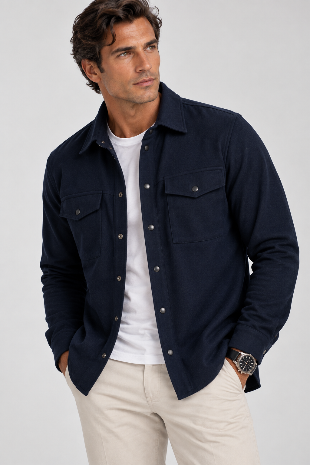 A man modeling a dark navy blue Atlas Overshirt over a white t-shirt, paired with creme cargo pants , standing against a textured beige studio backdrop.