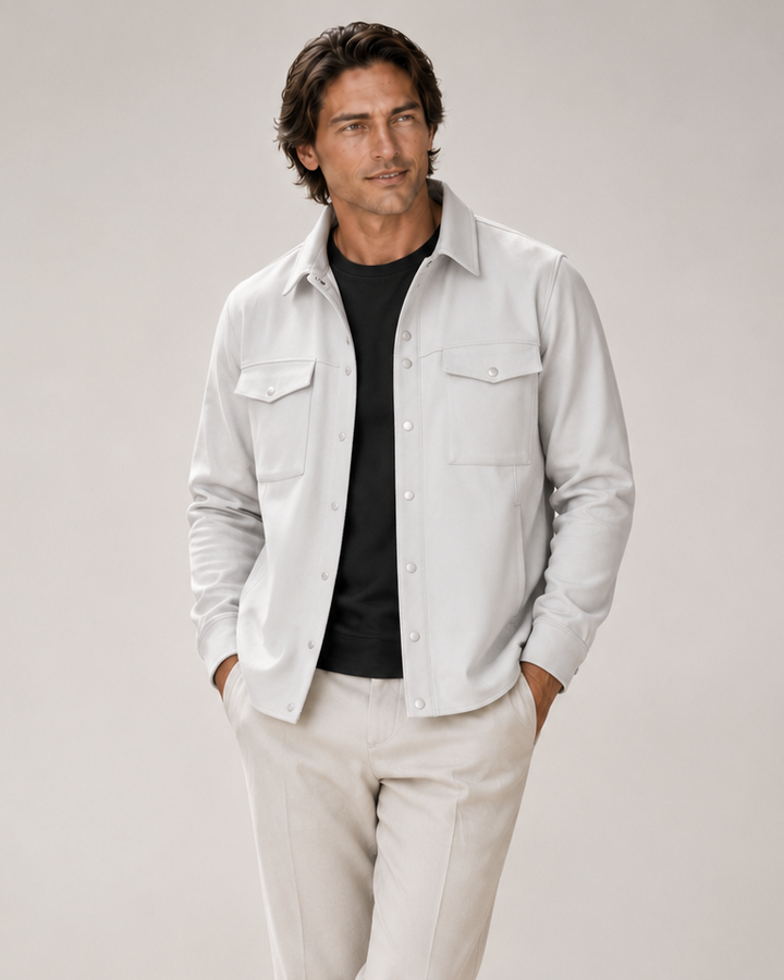 A man modeling the Atlas Over Shirt L button-down shirt jacket over a black Cinqo t-shirt, paired with light beige trousers and gray slip-on shoes, against a neutral light gray studio background.