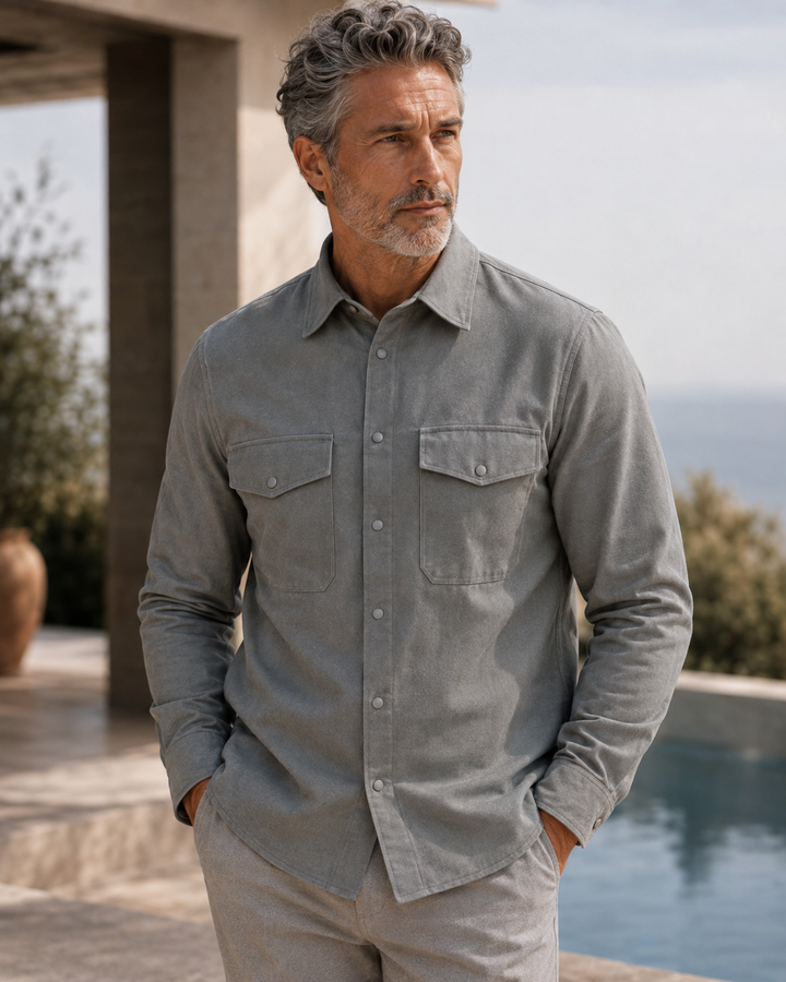 A man wearing an Atlas Overshirt with two chest pockets, standing outdoors near a pool and modern architecture.