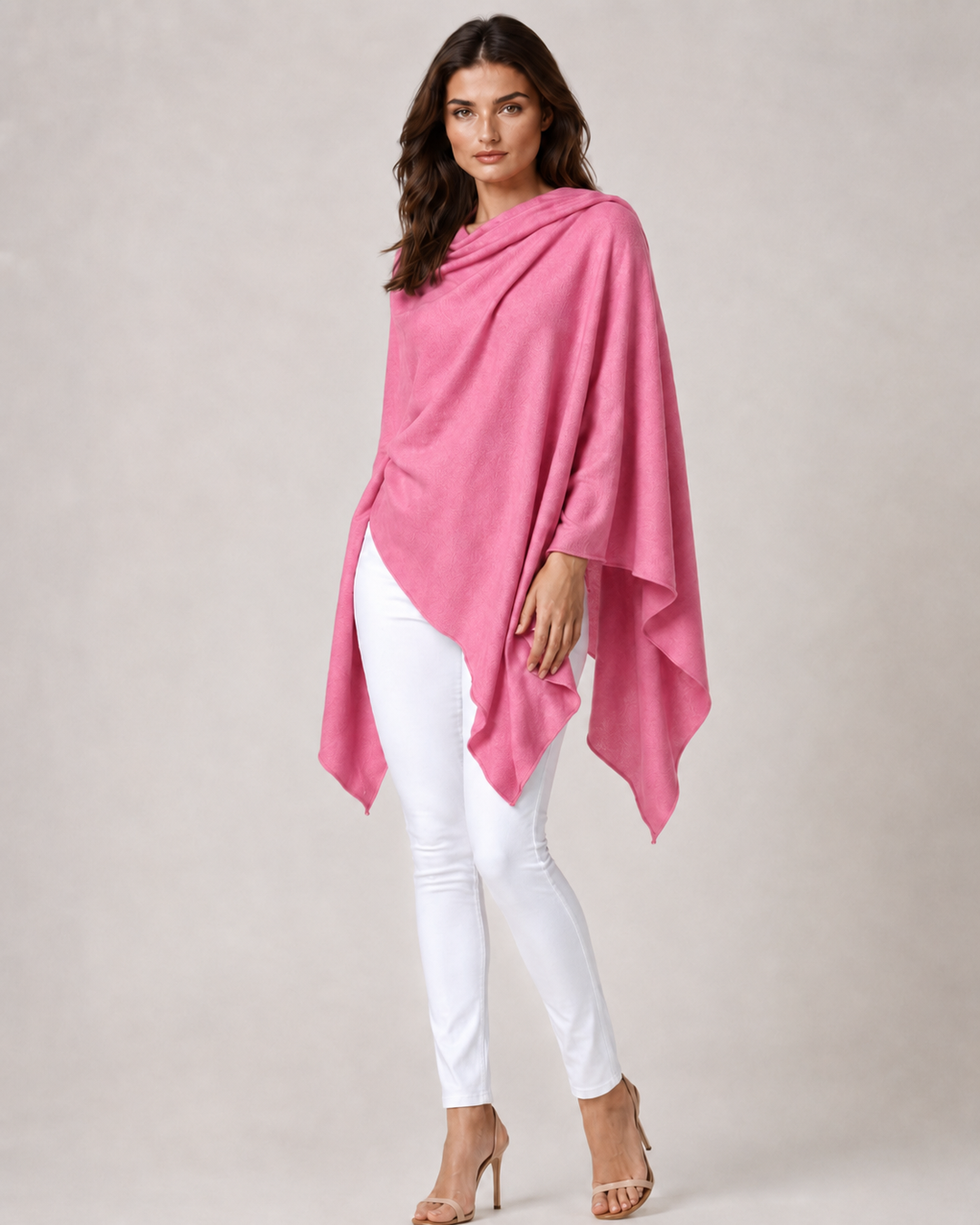 A woman modeling a draped berry wrap over a white top and white skinny pants, standing against a plain light gray studio background.