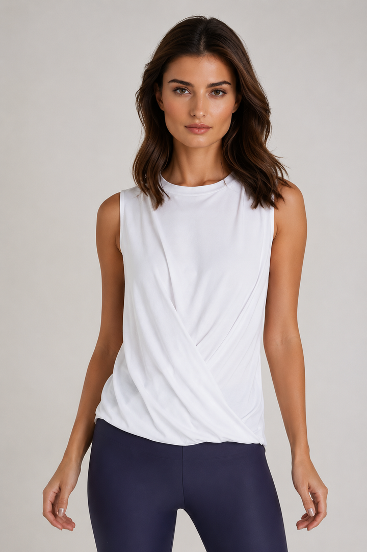 Woman wearing a Buki Boss Crew  white sleeveless tee and dark blue leggings on a plain background