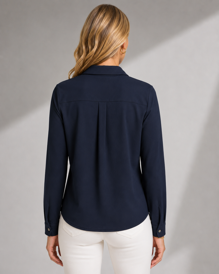 A woman viewed from the back wearing a Boss Lady navy blue long-sleeve blouse and white pants, standing against a light gray studio background with soft diagonal shadows.