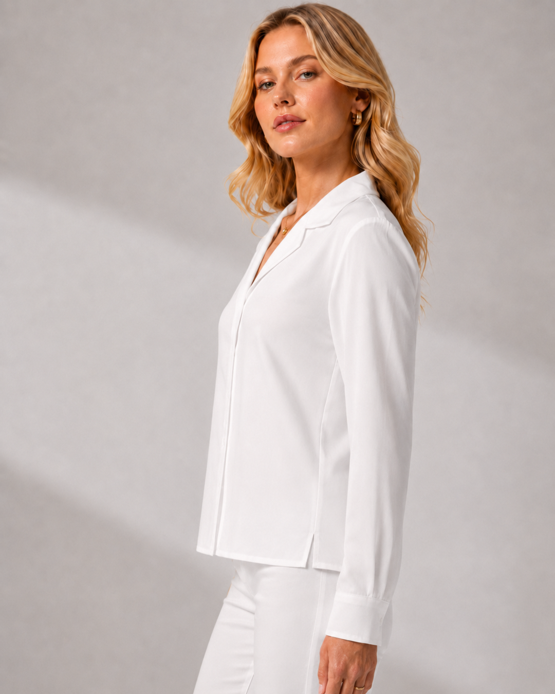 A woman wearing a Boss Lady white long-sleeve collared blouse and matching white trousers, photographed in profile against a light gray studio background.
