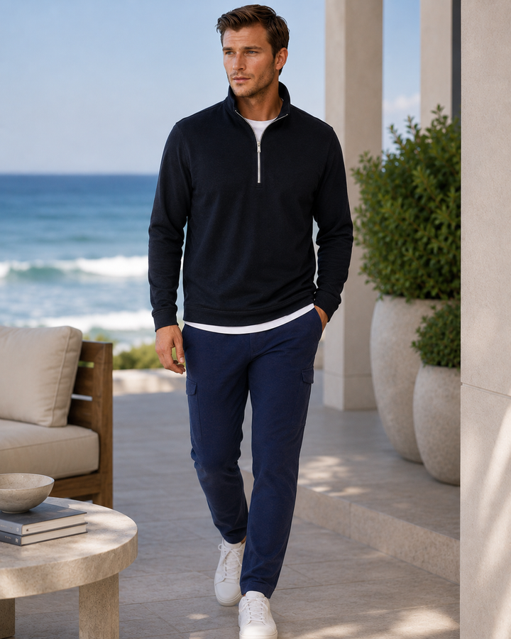 Man in Black Cinqo Half ZIp  and Hiogh Five pants and Cinqo Long Sleeve T-shirt walking outdoors with ocean view