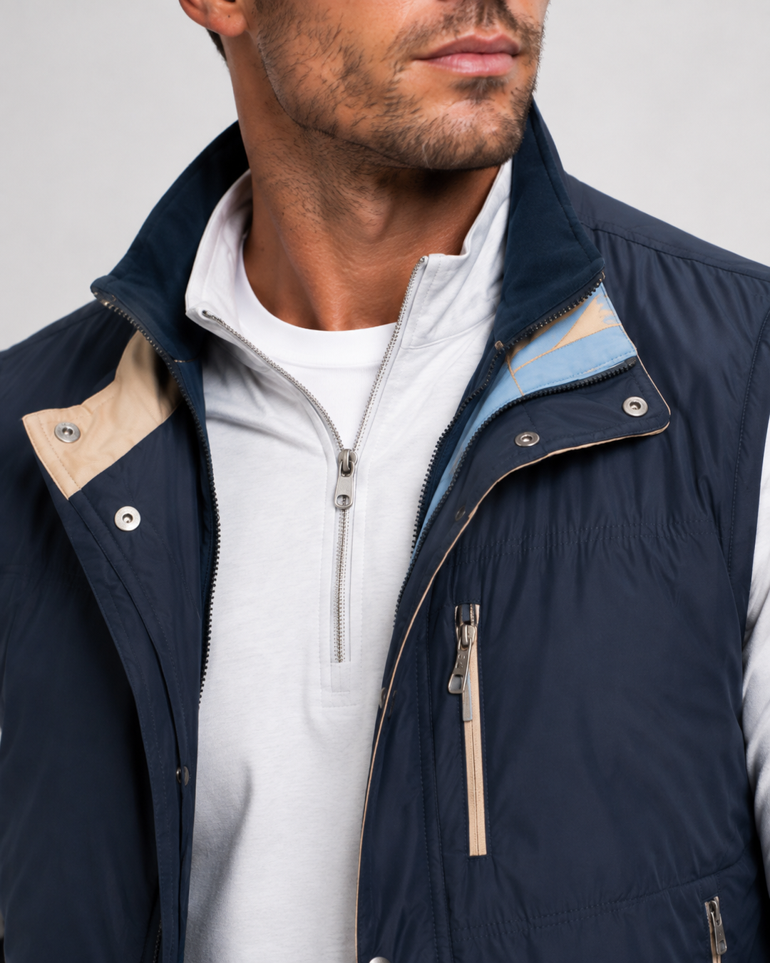 A close-up of a man wearing a navy blue Buki Tech zip-up vest over a white half-zip shirt. The vest features beige contrast panels on the shoulders and collar, and a light blue inner lining visible at the collar.
