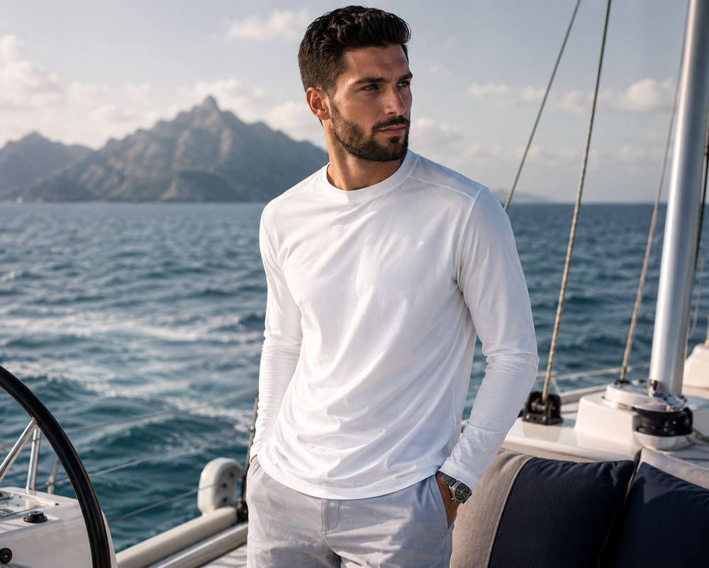 Man wearing Buki Cinqo Long Sleeve T-Shirt in white standing on a sailboat with mountains and ocean in the background