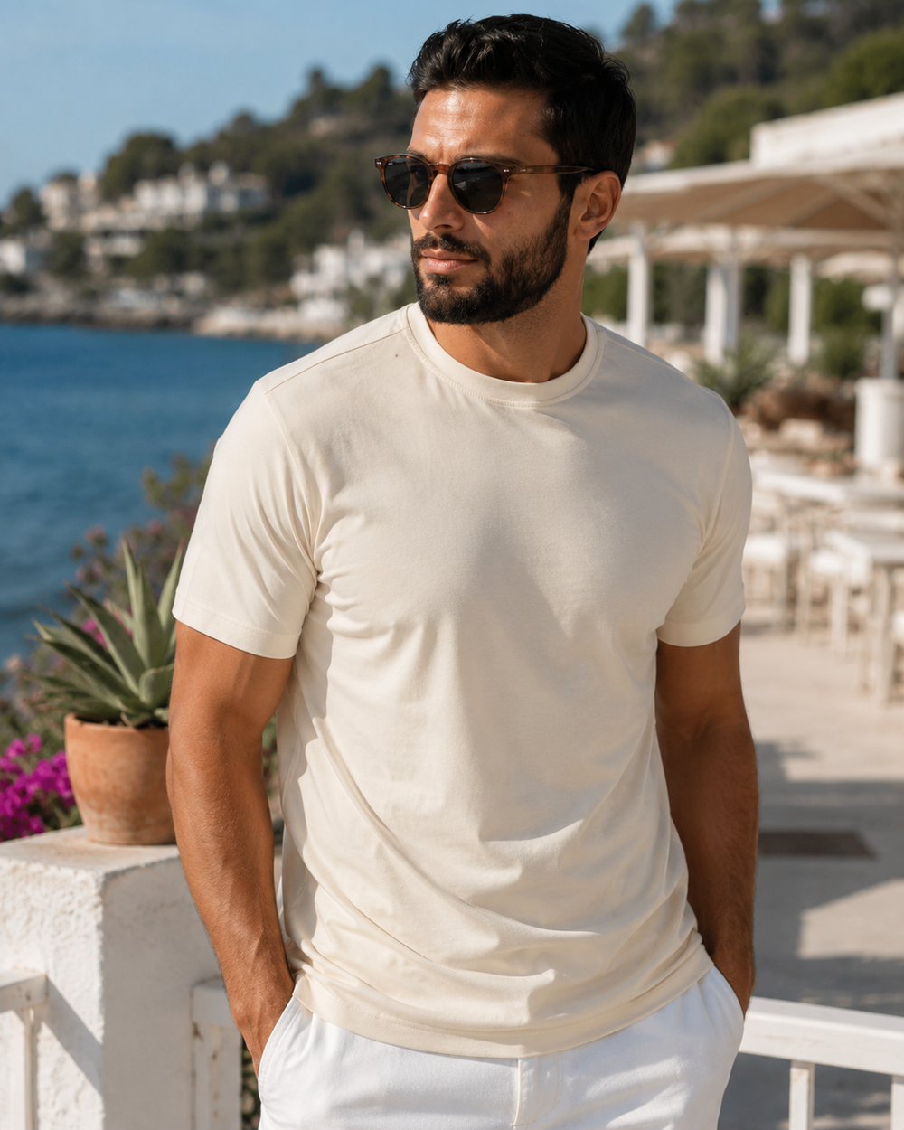 Man wearing sunglasses and a Buki Cinqo Maize T-Shirt by a waterfront with greenery and buildings in the background.