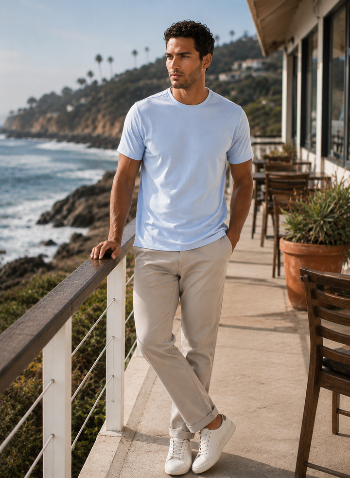 Man standing on a deck by the ocean wearing a Cinqo T-Shirt In French Blue and beige pants.