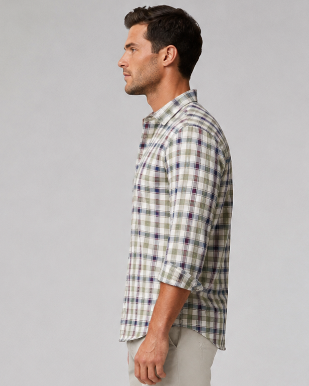 A man in profile wearing a Latitude long-sleeve plaid button-down shirt in beige, green, and white, paired with light beige trousers and beige loafers, standing against a light gray studio background.