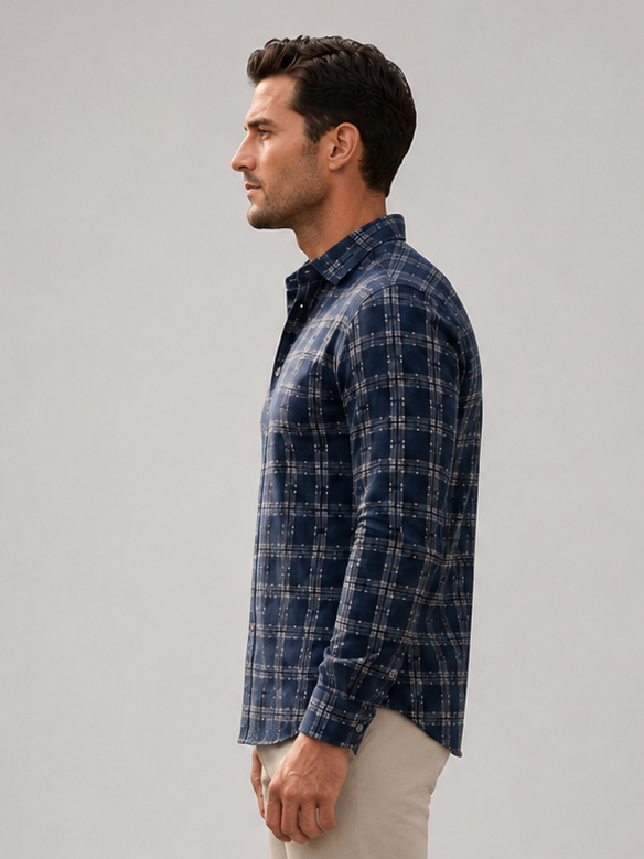 A man in profile wearing a Buki Latitude button-down shirt, beige trousers, and dark brown dress shoes, standing against a neutral light gray studio background.