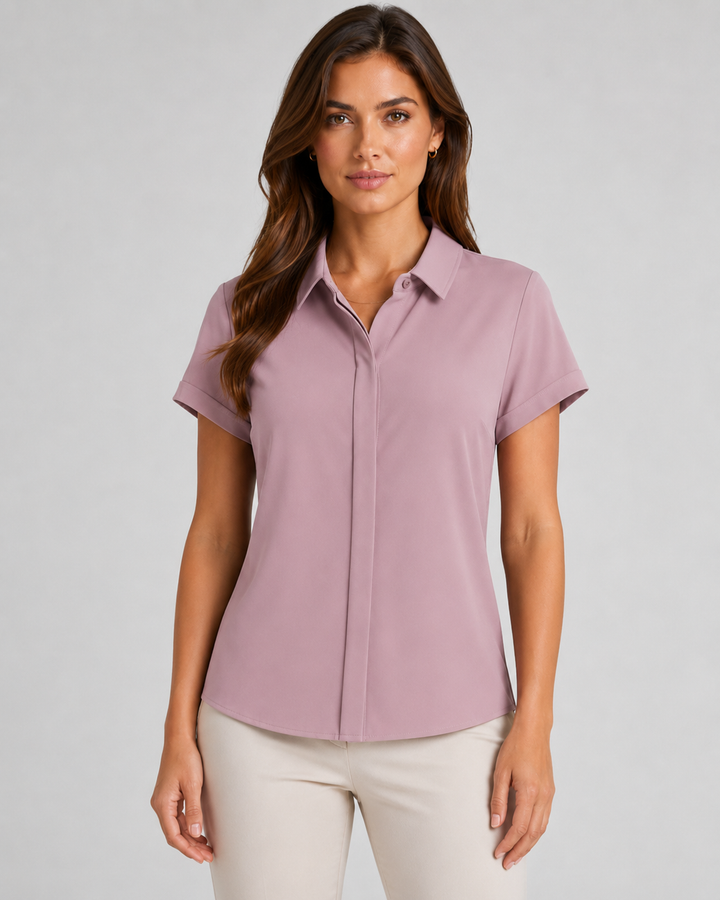 A woman modeling a maven short-sleeve button-up shirt in dusty rose, paired with light beige pants, against a solid light gray studio background.