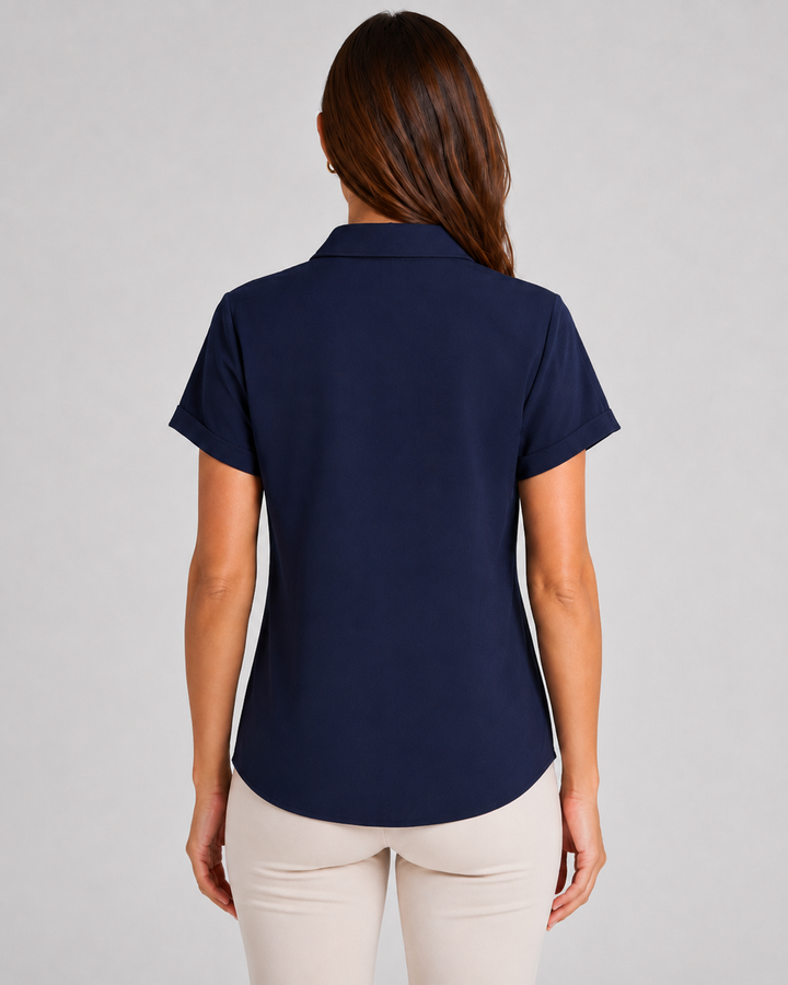 A woman viewed from the back wearing a short-sleeve maven in navy blue polo shirt and light beige pants, set against a plain light gray studio background.