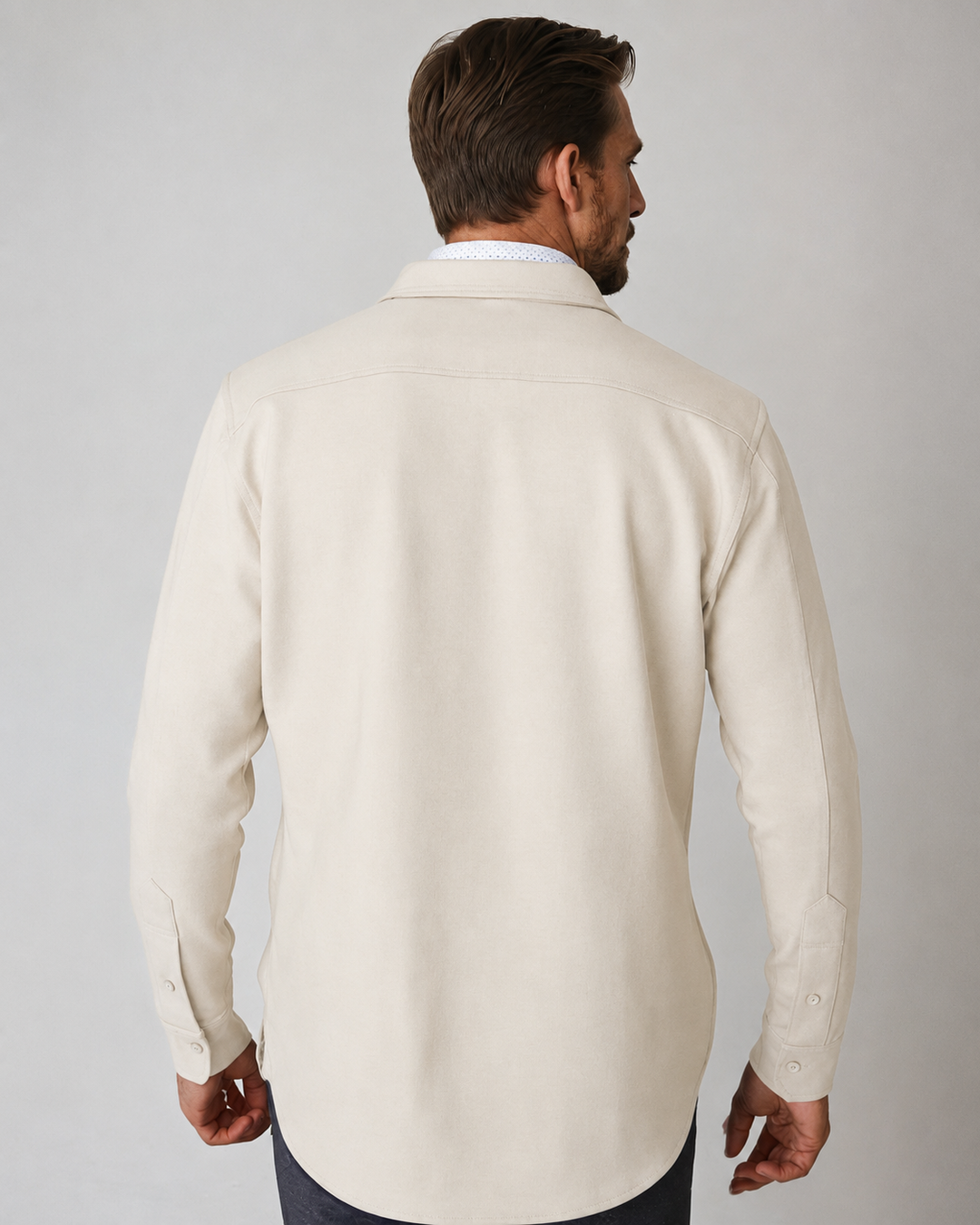 A man viewed from the back wearing an Atlas Over Shirt in Birch long-sleeve birch button-down shirt, set against a plain light gray studio background.