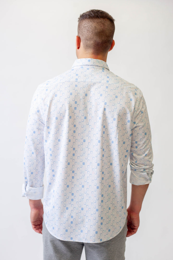 Man wearing a light-colored patterned shirt and gray pants against a white background