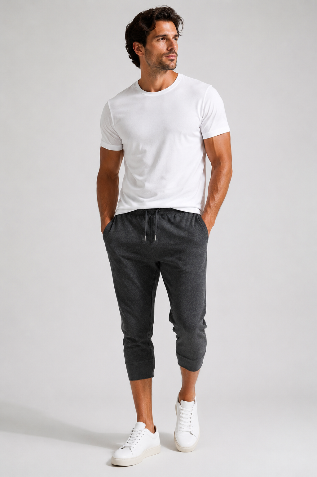 A man modeling a white Cinqo short-sleeve crewneck t-shirt and dark gray Scrimmage jogger pants with white sneakers, standing against a light gray studio background.