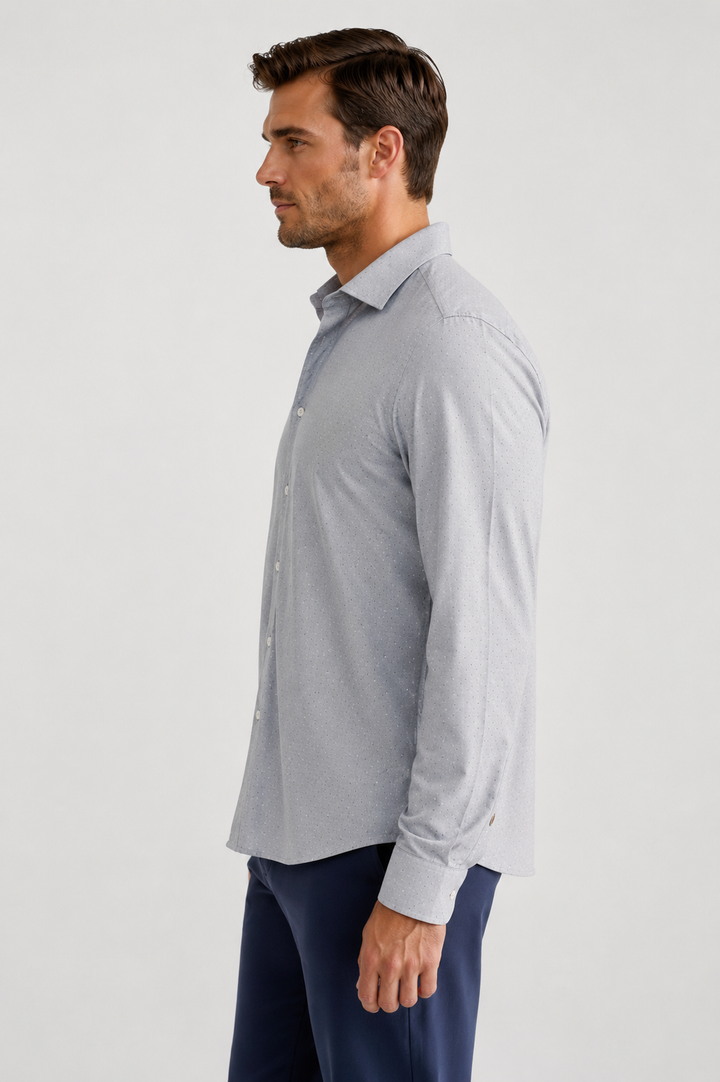 A man in side profile wearing a Studio Dot Silver long-sleeve button-down shirt and navy trousers, photographed against a plain light gray studio background.