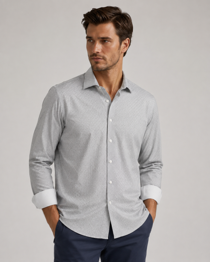 A man wearing a Studio Shot Silver long-sleeve button-down shirt with a subtle micro-pattern, paired with navy blue trousers, photographed against a neutral light gray background.