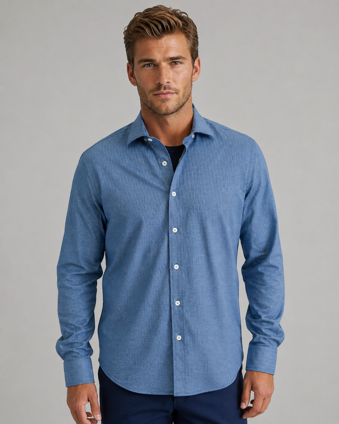 A man wearing a Buki Studio Dot long-sleeve button-down shirt with a subtle textured pattern in Navy, paired with dark navy pants, photographed against a solid gray studio background.