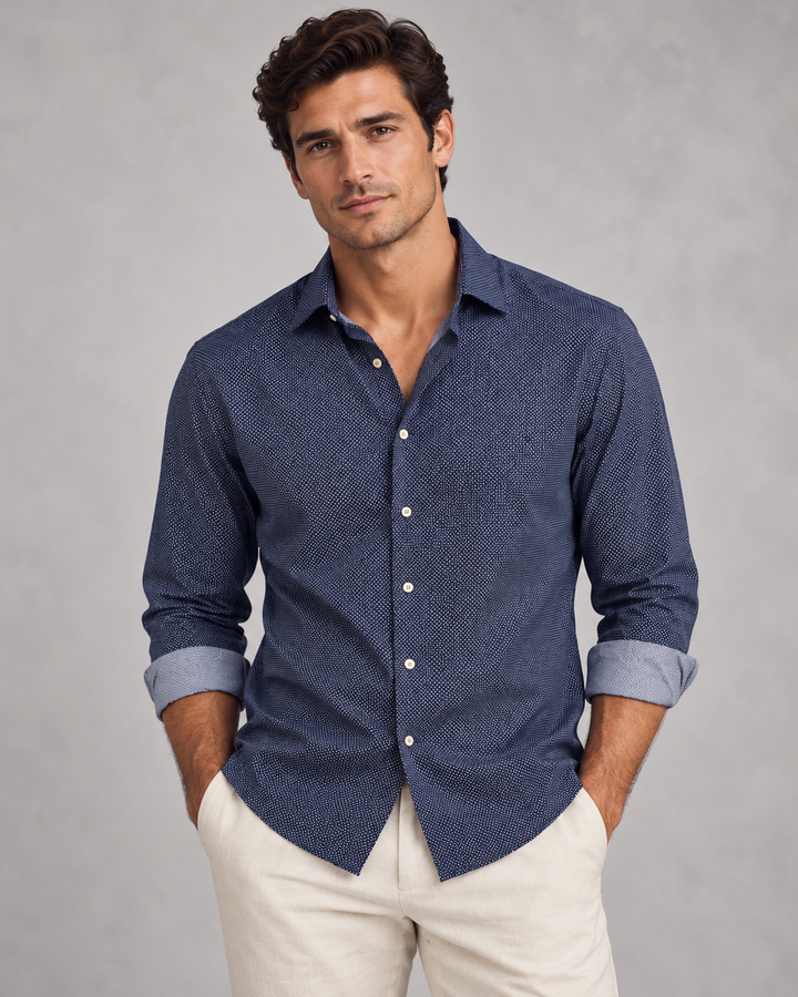 A man wearing a Buki Studio Dot long-sleeve button-down shirt with a subtle textured pattern in Navy, paired with dark navy pants, photographed against a solid gray studio background.