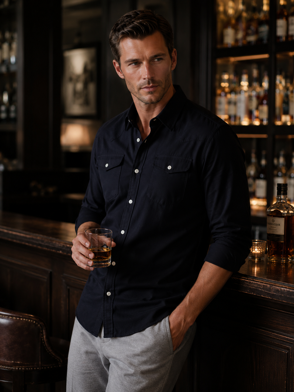 Man holding a glass of whiskey in a bar setting with Western Shirt in Black and  Buki Heatehr Gray High Five Pant