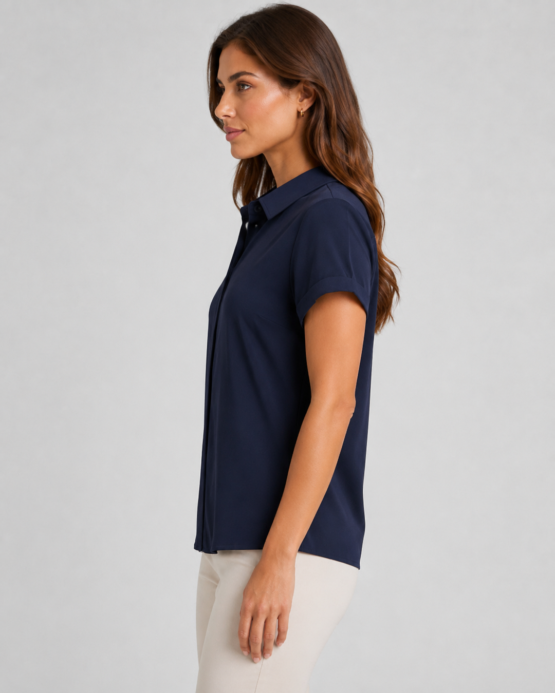 A woman shown in side profile wearing a short-sleeve navy Maven button-up shirt and light beige pants, photographed against a plain light gray studio background.